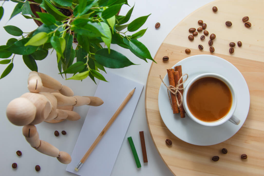 top-view-cup-coffee-with-wooden-robot-plant-coffee-beans-dry-cinnamon-paper-pencil-platform-white-surface-horizontal